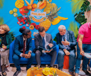 Rody TOLASSY et des élus lors d'un événement Philibon, discutant sur un canapé bleu devant un mur décoré de fruits tropicaux